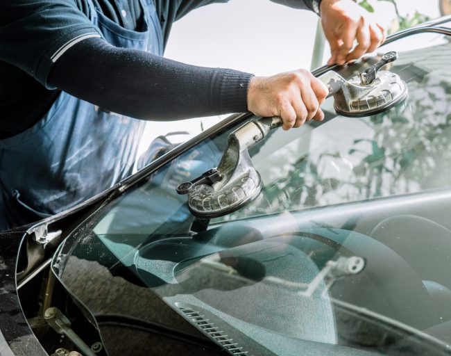 Mechanics man changing the broken windshield and automobile windshield or windscreen replacement of white car in Auto Repair Shop